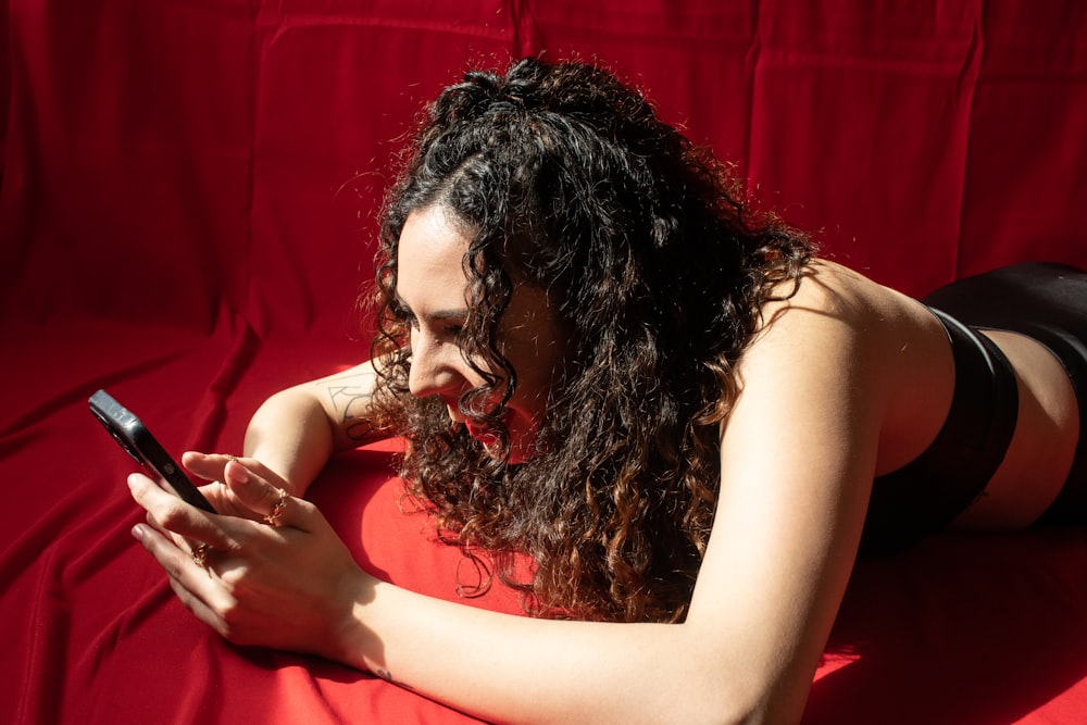 a woman laying on a red sheet looking at her cell phone