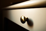 A close-up of a desk or drawer with a metallic knob, bathed in warm lighting that highlights its texture and shape. The background is slightly blurred, adding to the focus on the knob.