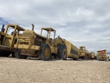 Wide shot of a fleet of heavy machinery parked in a dusty work yard.