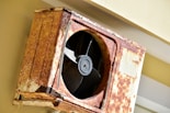 a rusted metal fan mounted to the side of a building