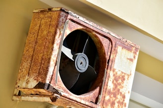 a rusted metal fan mounted to the side of a building