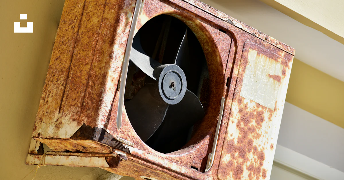 A rusted metal fan mounted to the side of a building photo – Free ...
