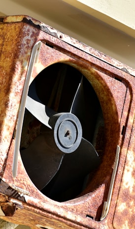 a rusted metal fan mounted to the side of a building