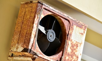 a rusted metal fan mounted to the side of a building