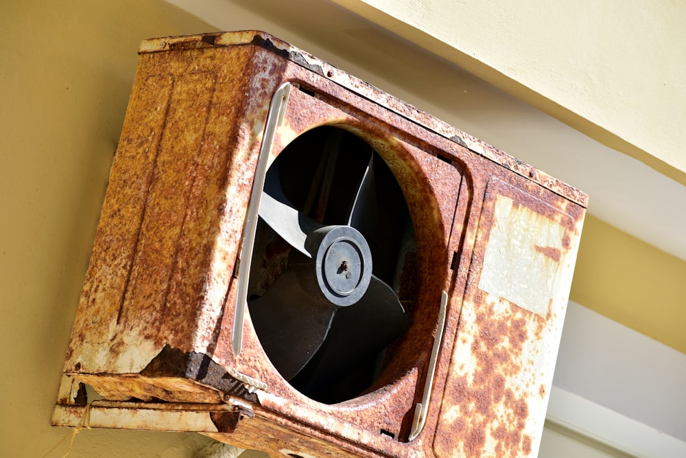 um ventilador de metal enferrujado montado ao lado de um edifício