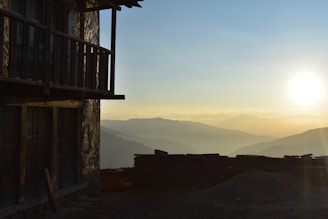 A rustic wooden balcony overlooking a quiet village street at sunset.