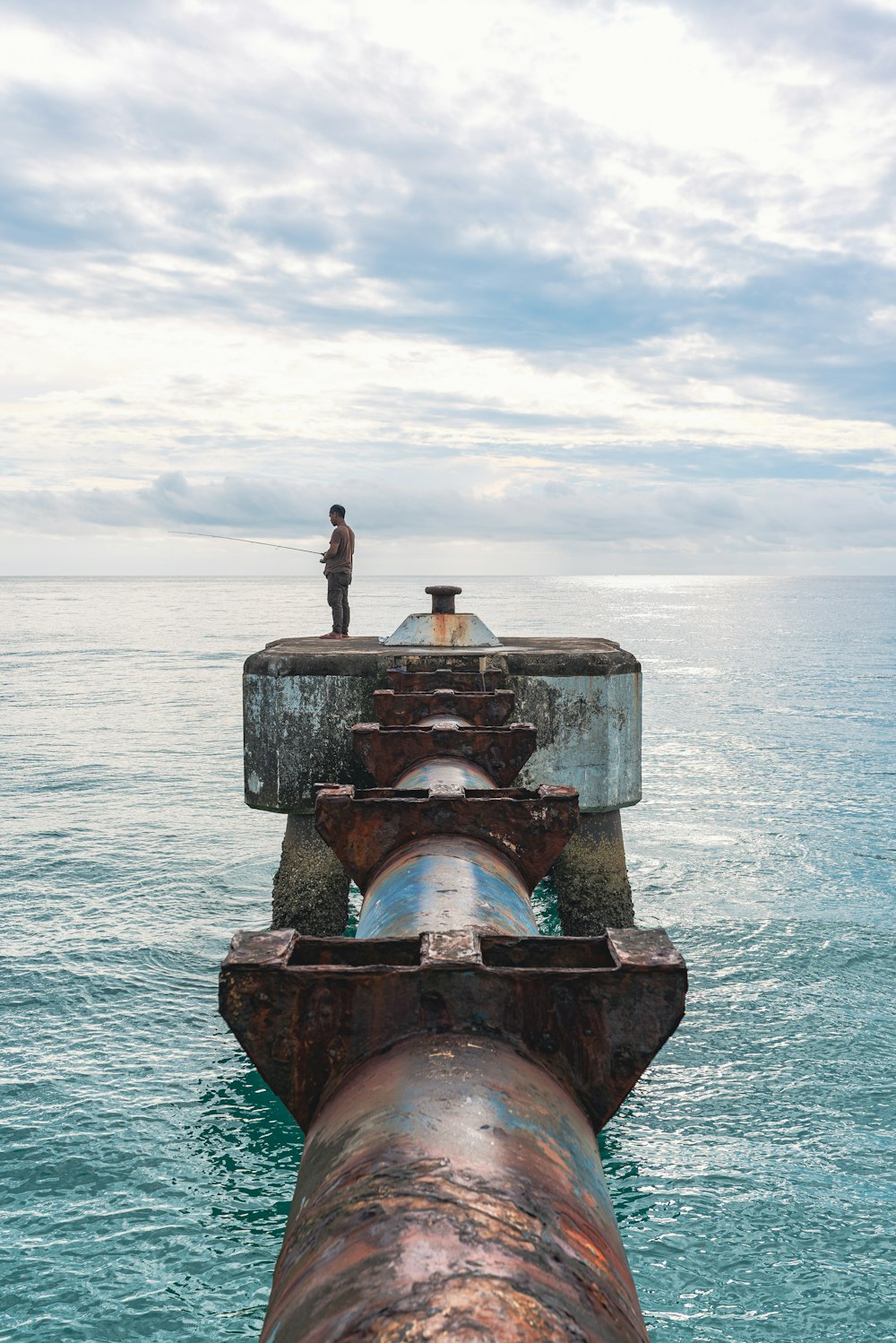 a man standing on top of a large pipe in the ocean