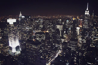 A nighttime view of a busy financial district with illuminated skyscrapers.