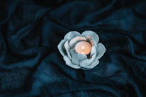 Close-up of a terracotta tea light holder with a flickering candle inside, set against a soft off-white background.