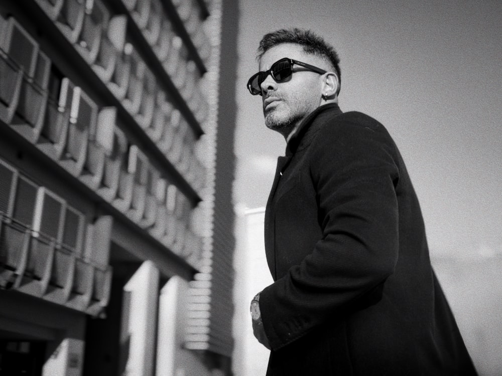 a man in a coat and sunglasses standing in front of a building