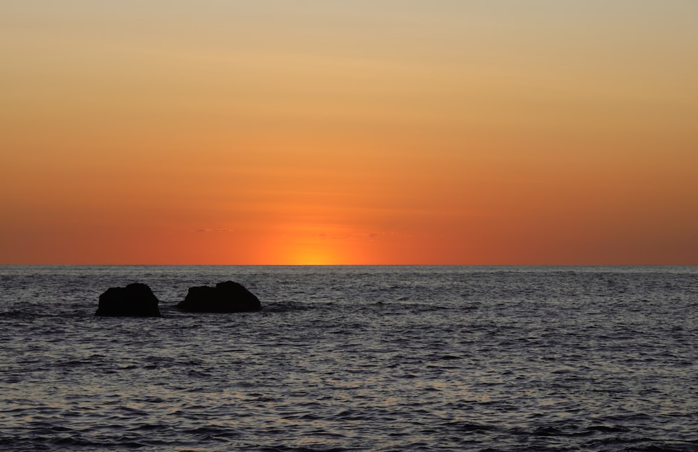 the sun is setting over the ocean with rocks in the water