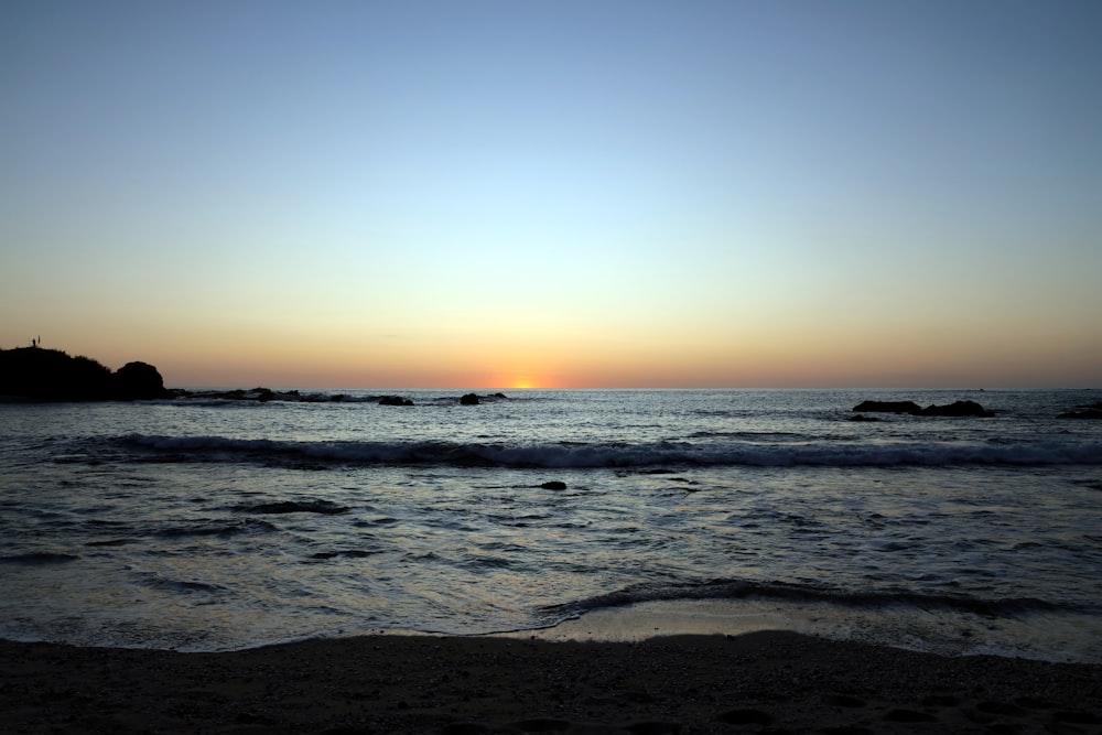 the sun is setting over the water at the beach