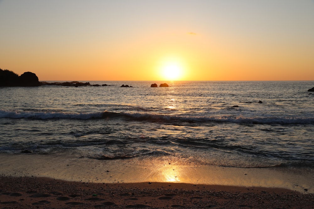 the sun is setting over the water at the beach