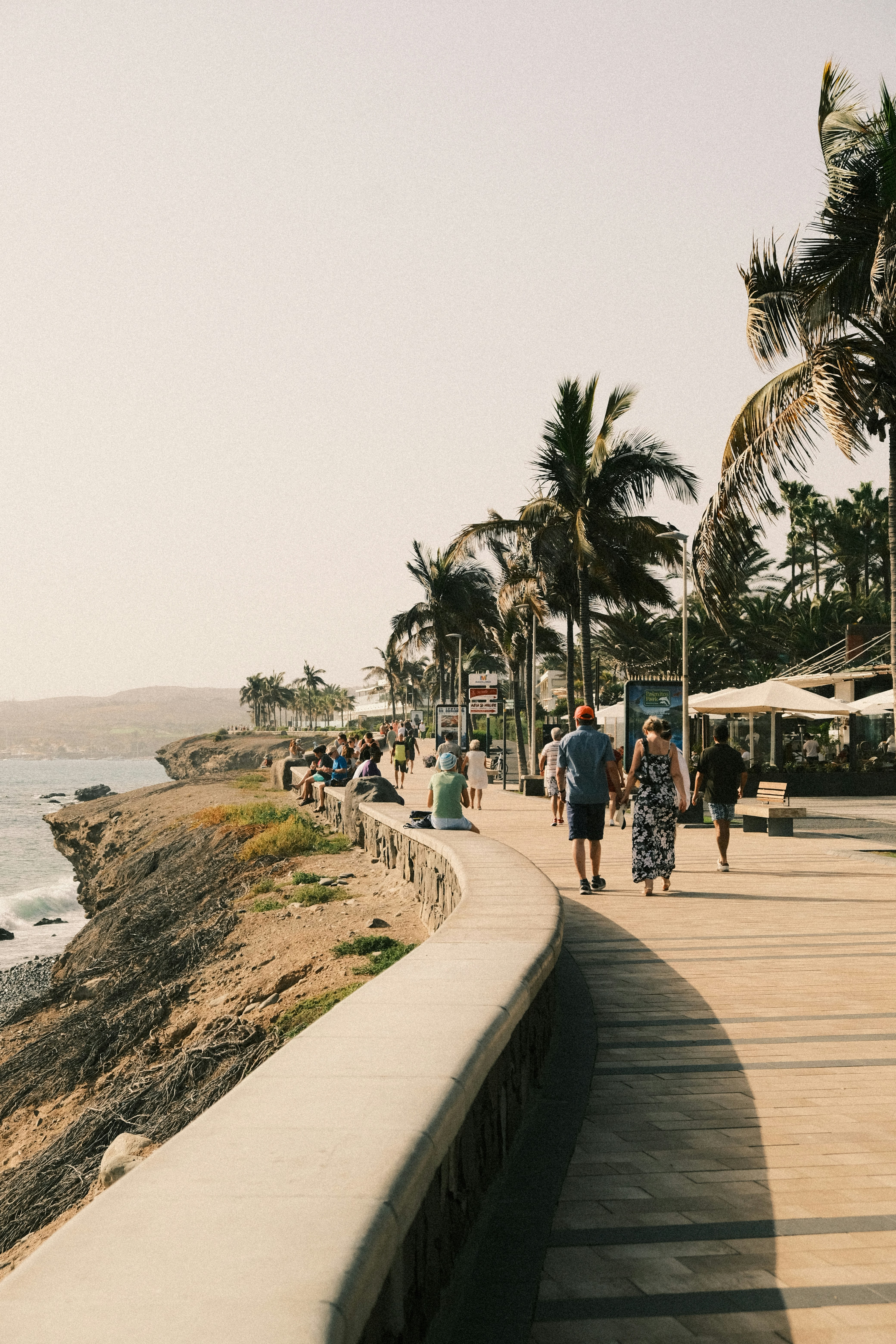a group of people walking down a sidewalk next to the ocean