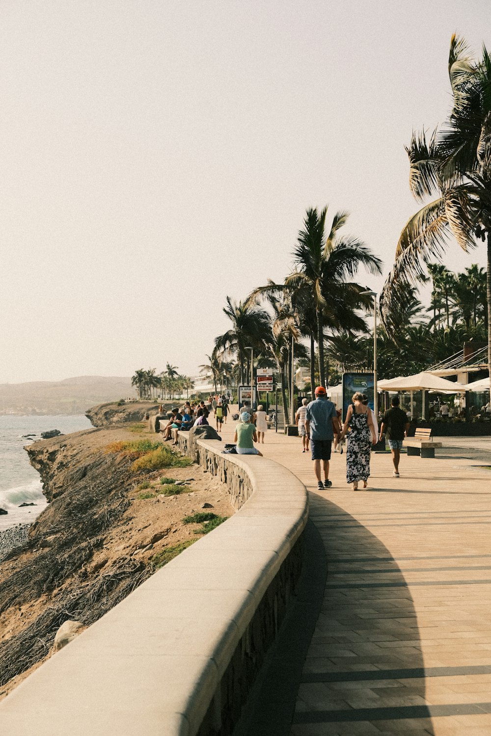 a group of people walking down a sidewalk next to the ocean
