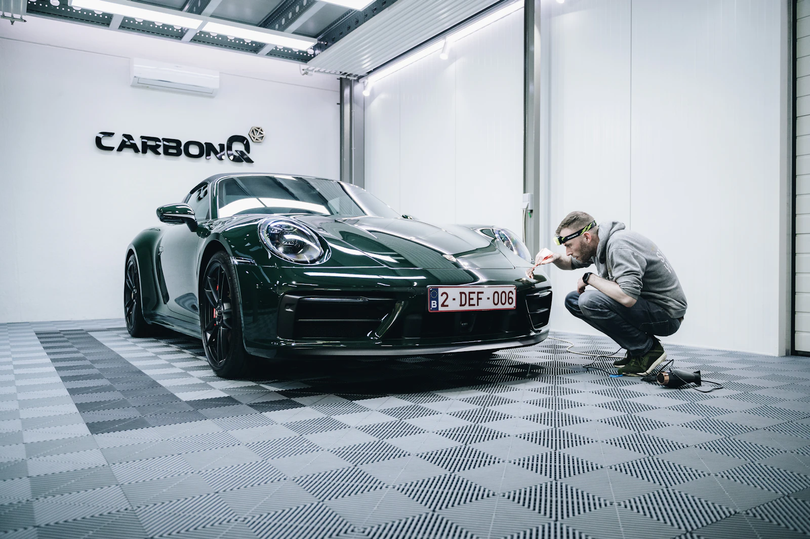 Technician detailing a dark green Porsche 911 in a detailing studio