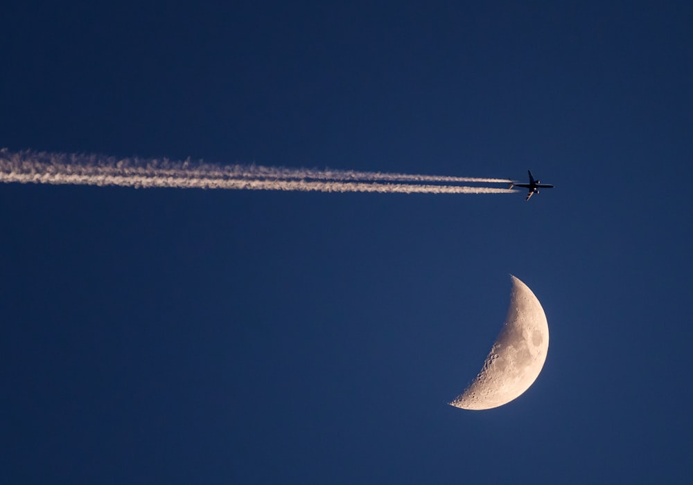a plane flying past a half moon in the sky