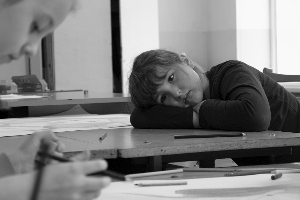 a young girl laying on a table with a pencil in her hand