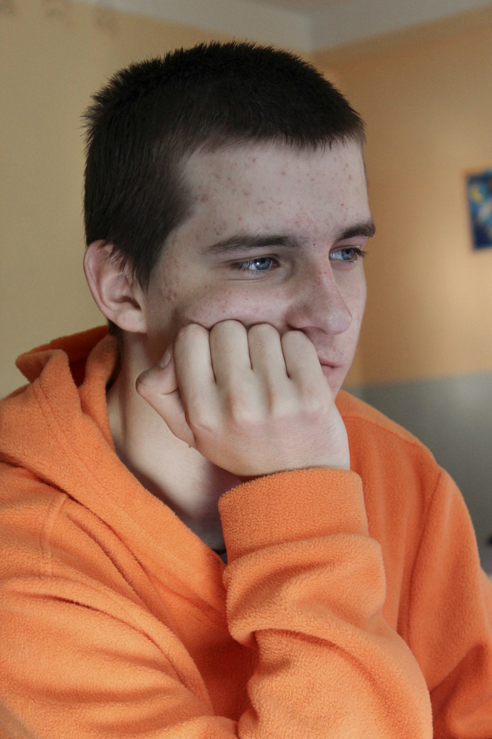a young man in an orange sweatshirt looks at the camera