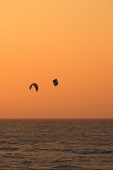 A vibrant sunset over the ocean with kiteboarders gliding across the water.