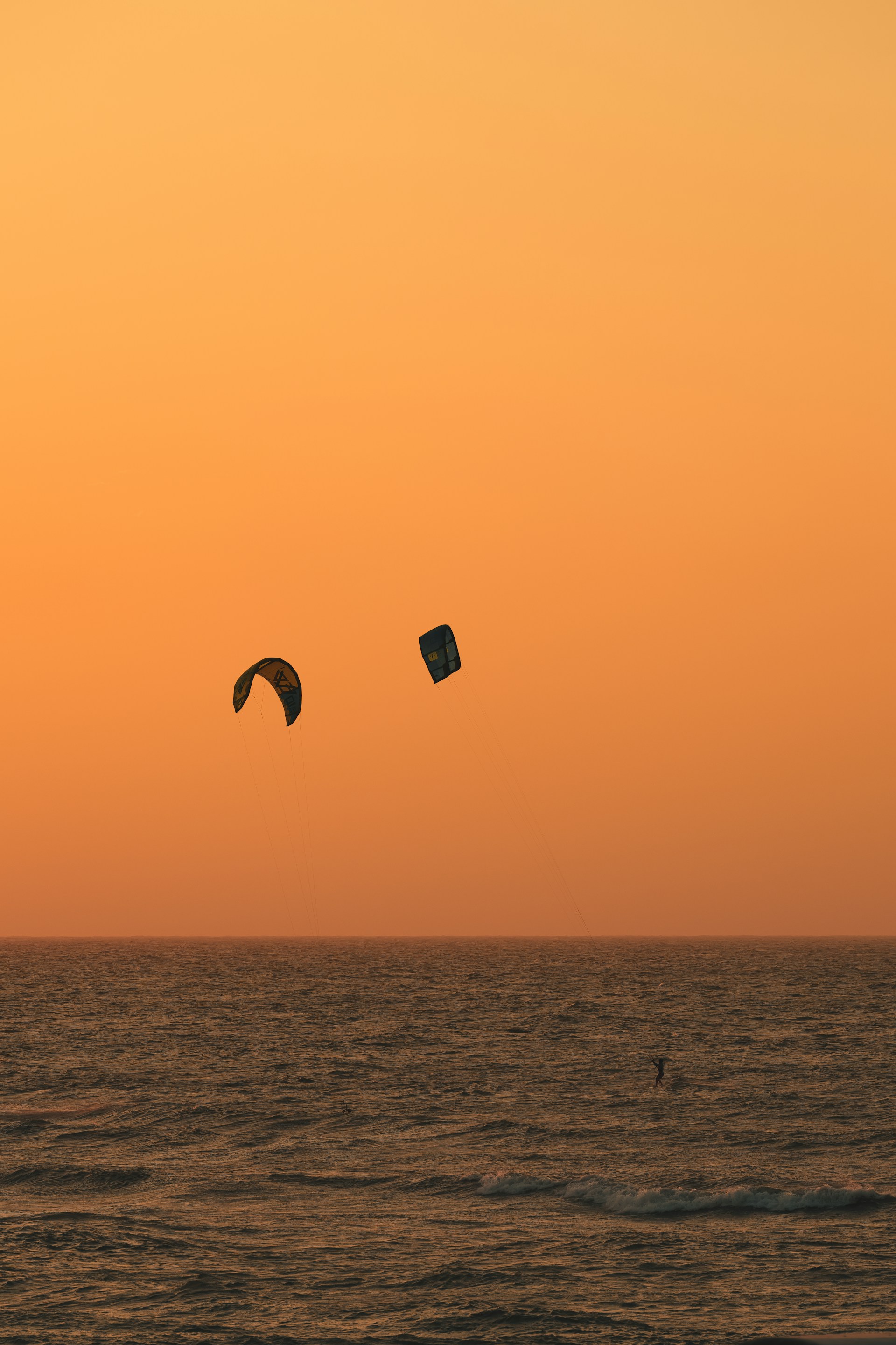 A vibrant sunset over the ocean with kiteboarders gliding across the water.