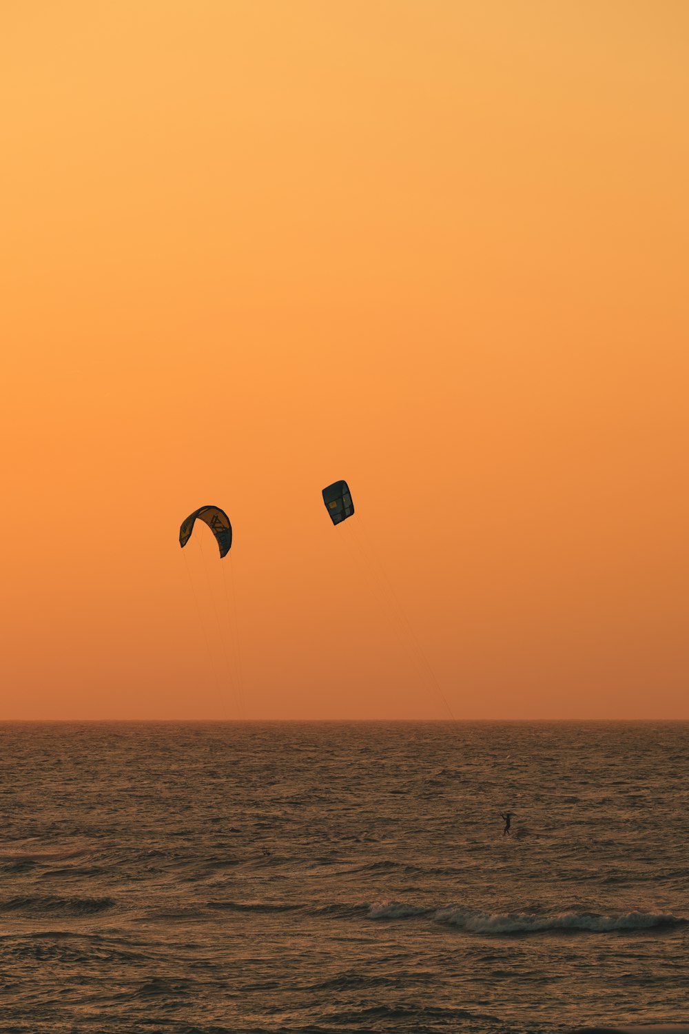 a couple of kites flying over the ocean at sunset