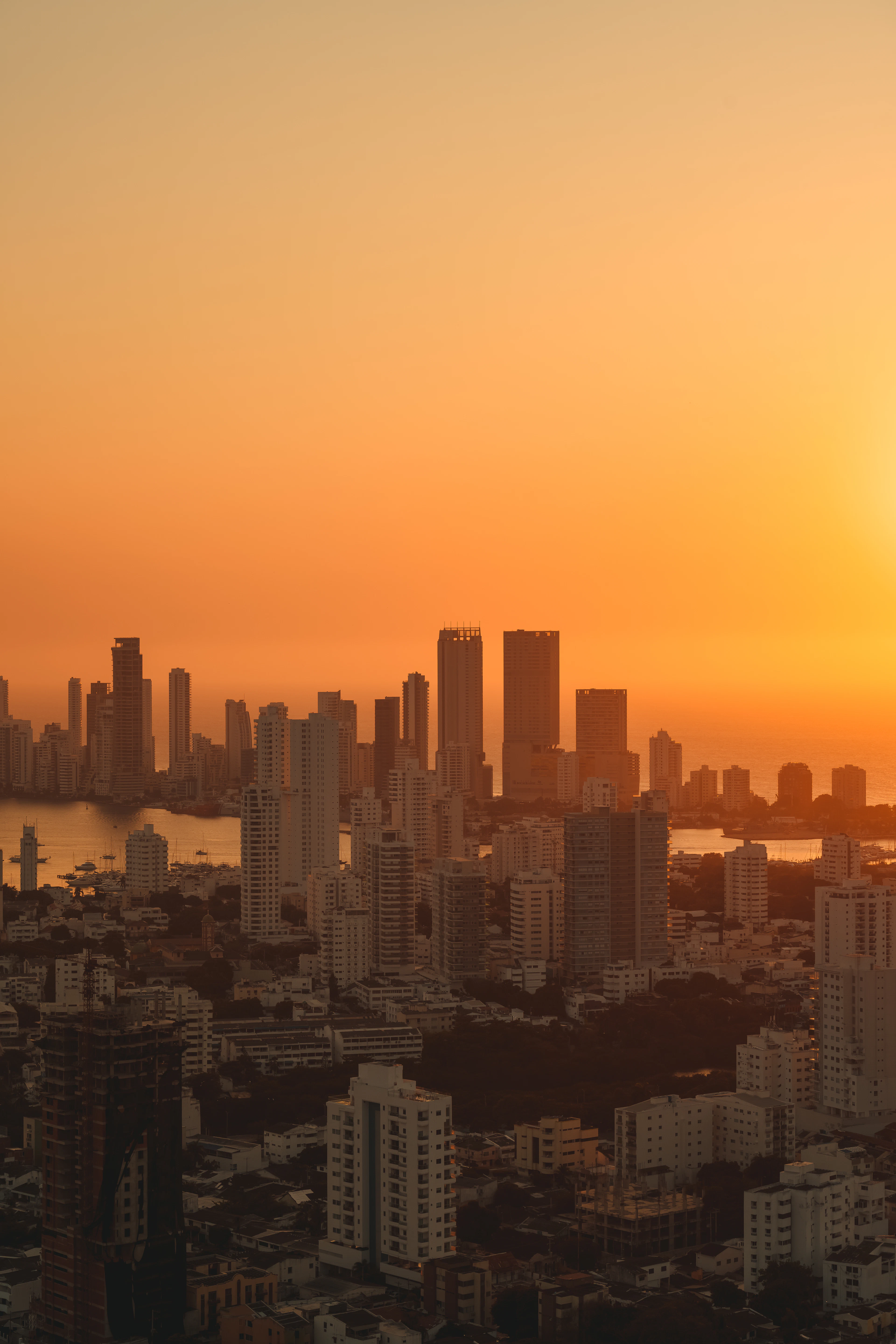 Cartagena's skyline towers are silhouetted against a blazing orange aerial sunset.