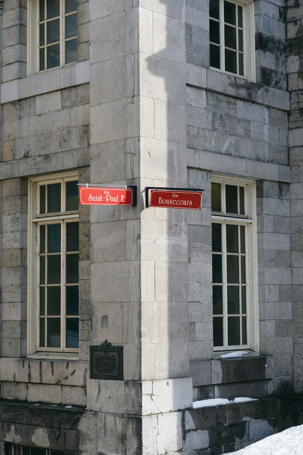 two red street signs on a stone building