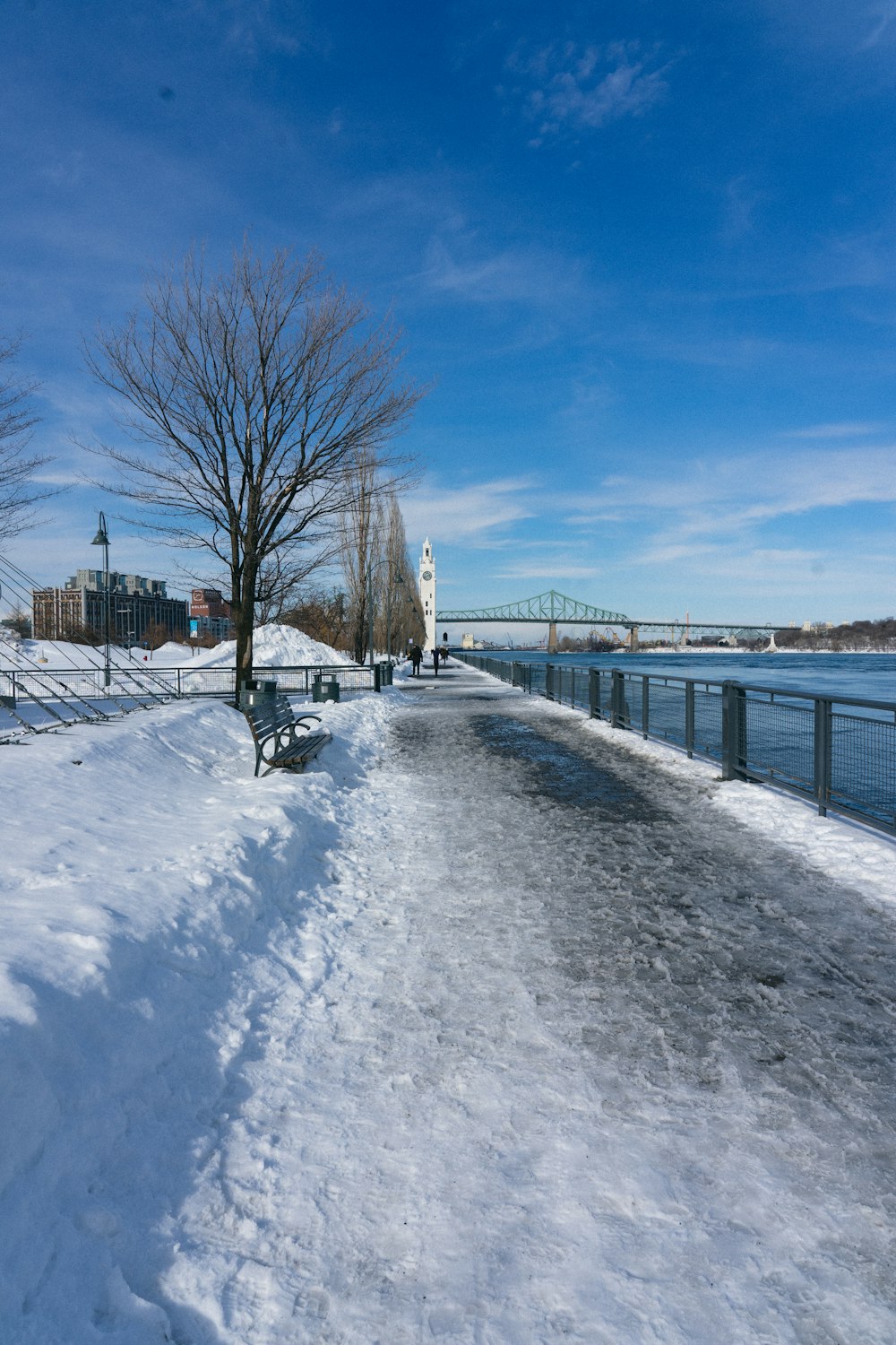 a park bench covered in snow next to a body of water