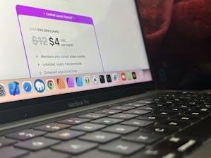 A close-up view of a MacBook Pro showing a section of the screen and keyboard. The screen displays a marketing offer for a subscription service with a limited launch special price. Various app icons are visible on the dock at the bottom of the screen.