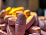 A close-up view of a pile of oval-shaped pills with imprinting on the surface, under warm lighting.