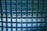 A grid of translucent glass blocks, each with a slightly convex surface, casting reflections and light patterns. The glass blocks are arranged in a uniform pattern, creating a mosaic-like effect with predominantly blue hues.