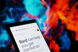 A smartphone screen displaying a web page from bard.google.com. The background is a vibrant and colorful abstract pattern, featuring swirling shapes in blue, red, and orange hues.