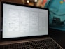 A laptop displaying a wireframe design for a website. The screen shows multiple pages with sections labeled for a landing page, product details, and about information. The background contains a blurred backpack.