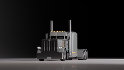 A large, shiny semi-truck with a prominent front grille is positioned on a reflective surface against a dark background. The truck features dual exhaust stacks and a sleeper cab design with several orange lights along the roofline.