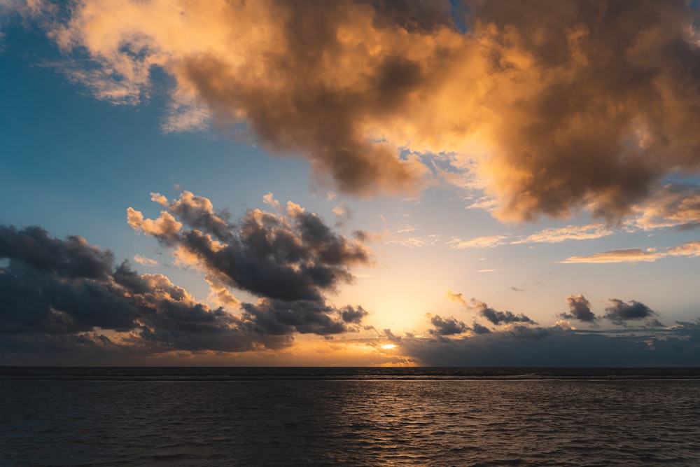 the sun is setting over the ocean with clouds in the sky