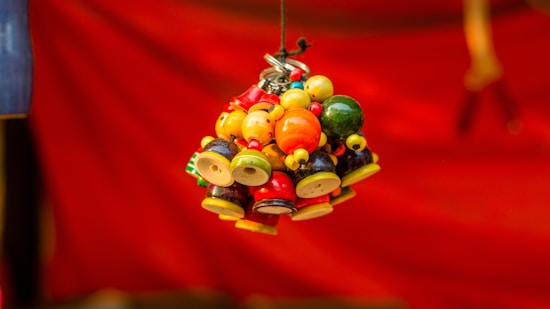 Colorful cluster of small, round decorative beads and bells hanging by a string against a blurred red background.