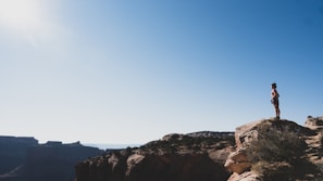 A lone traveler standing on a rocky cliff overlooking a sunrise-lit valley