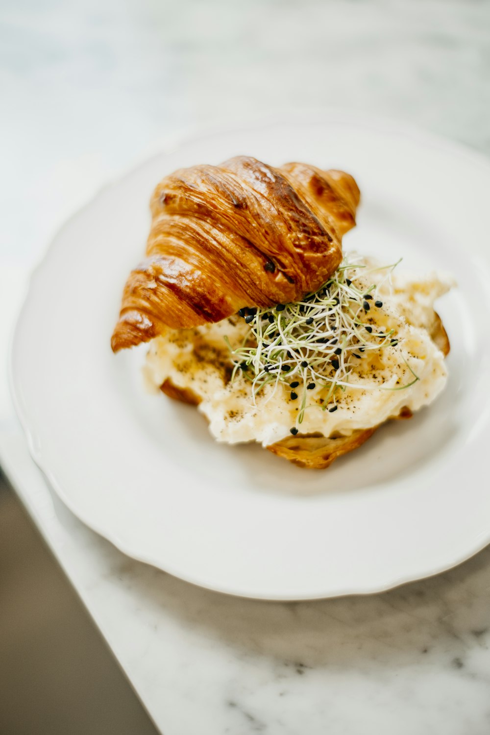 a white plate topped with a croissant and potatoes