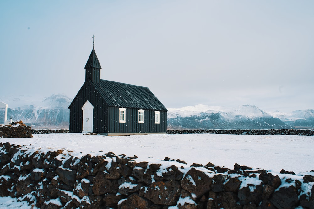 a small black church in the middle of a snowy field