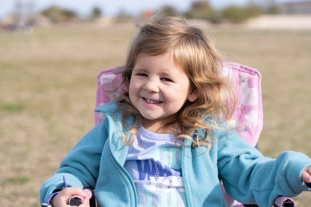 a little girl sitting in a pink chair in a field