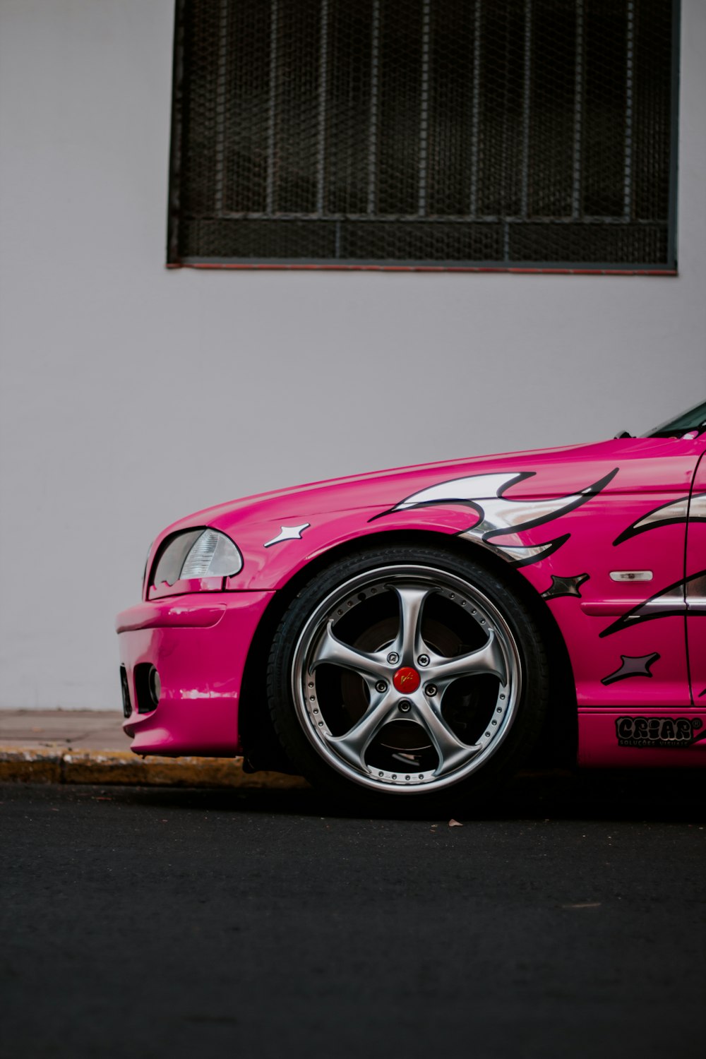 um carro esportivo rosa estacionado em frente a um prédio