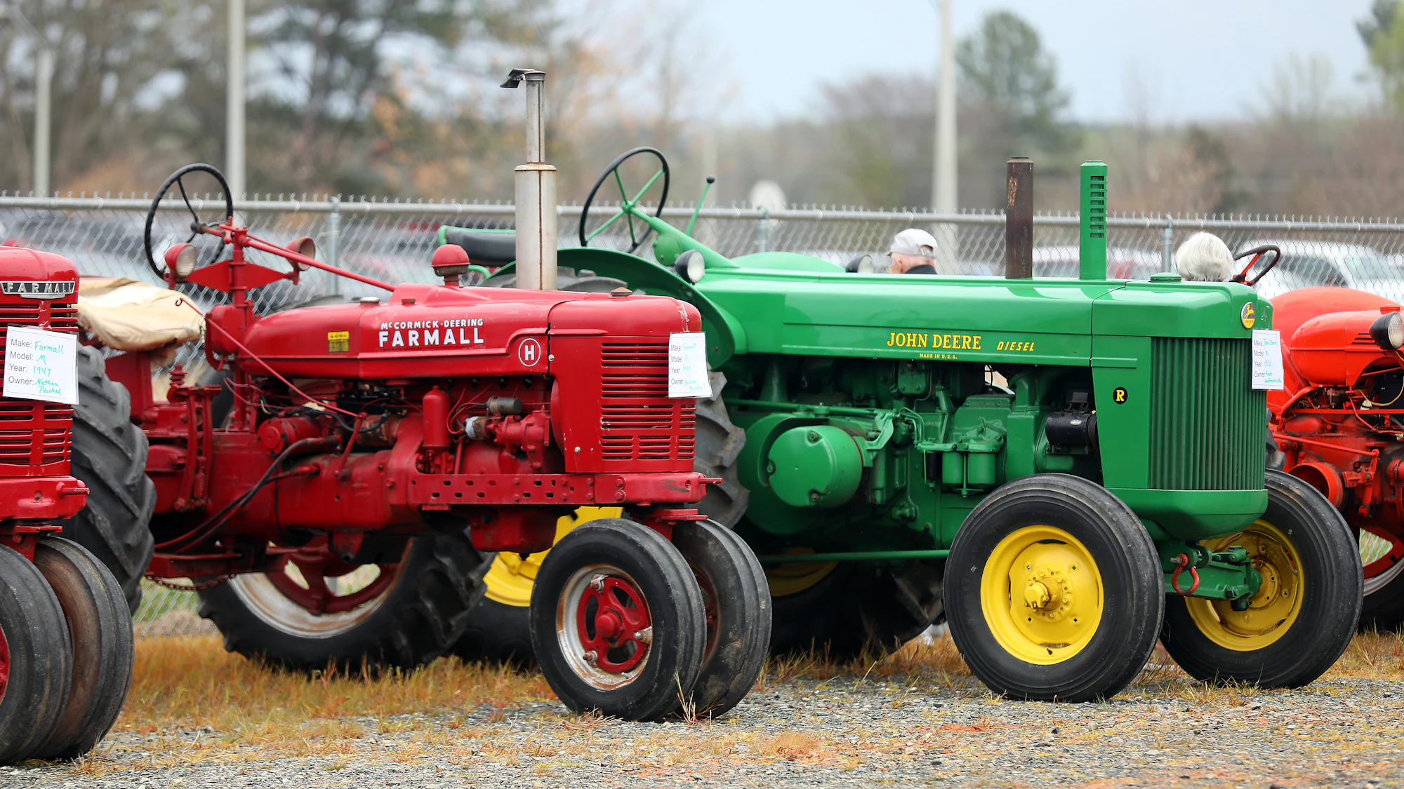 A row of red and green farm tractors lined up on a dealership lot.