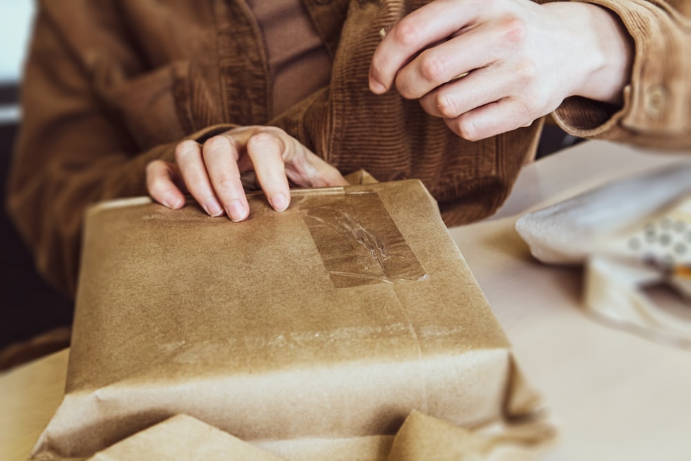 a person holding a brown paper bag on top of a table