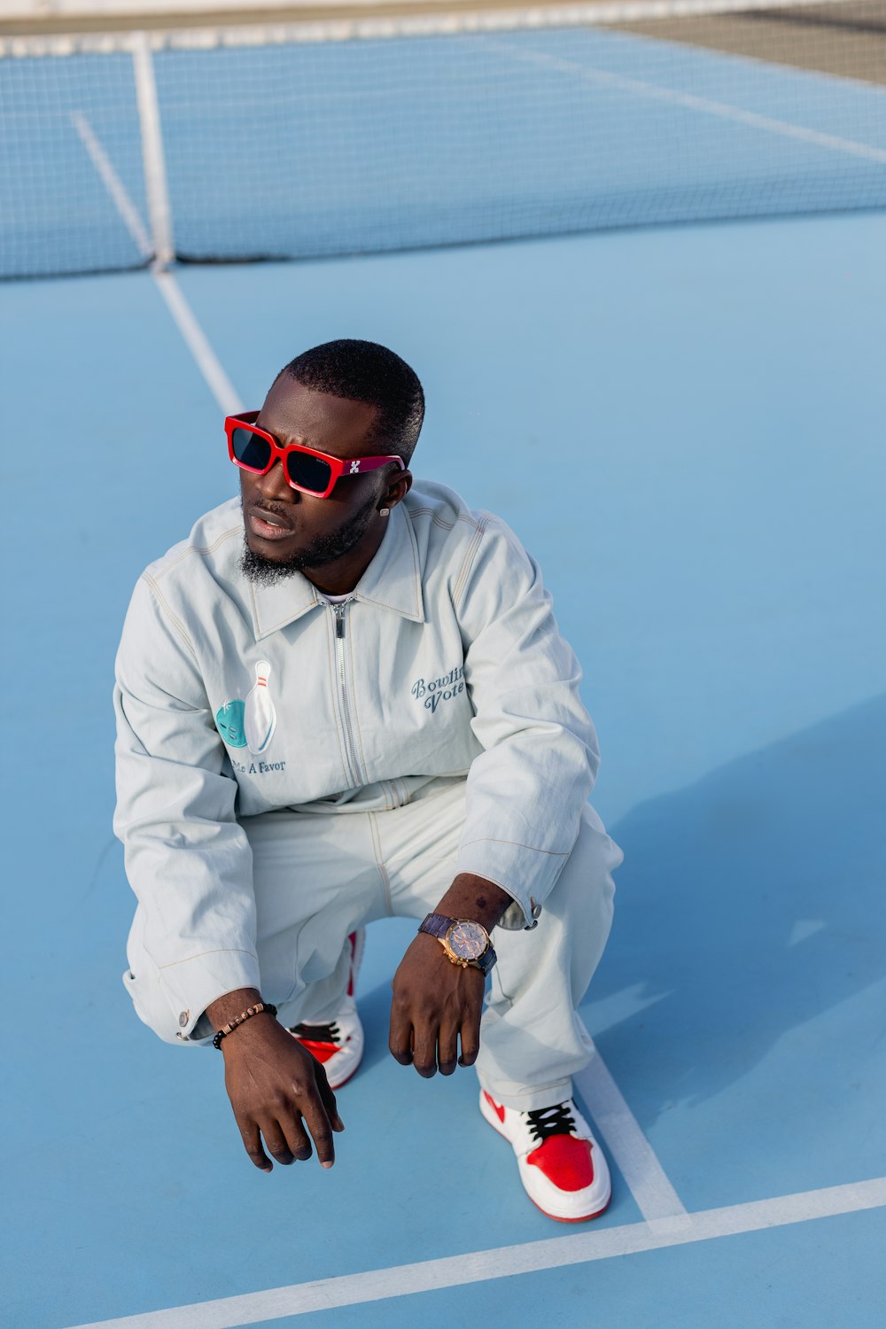 a man sitting on a tennis court wearing sunglasses