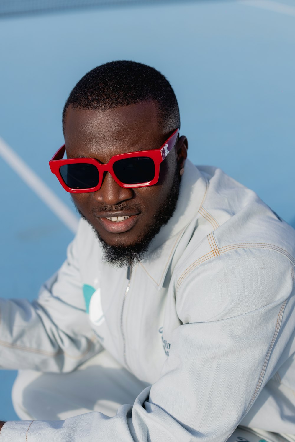 a man wearing red sunglasses sitting on a tennis court