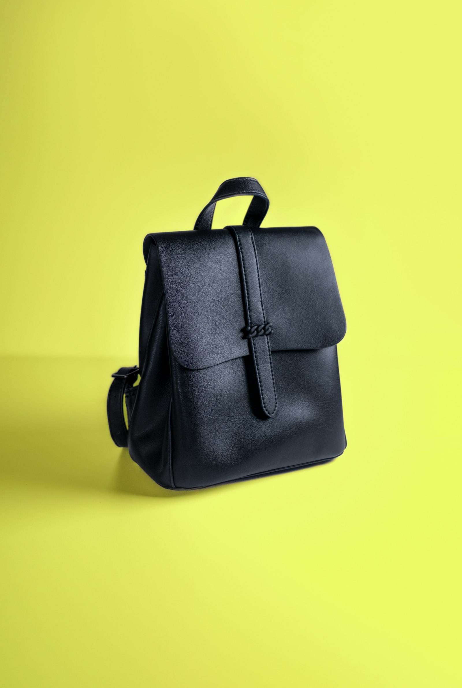 Un sac à dos noir à rabat, sur un fond jaune