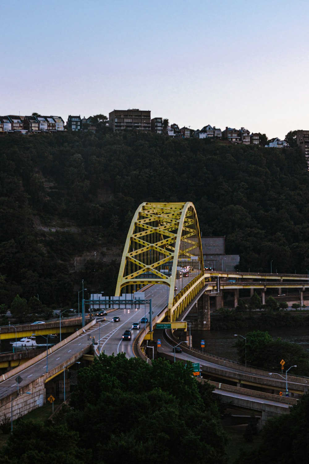 a yellow bridge crossing over a river next to a lush green hillside