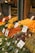 A vibrant market stall displays a wide array of fresh fruits and vegetables, including oranges, bananas, artichokes, carrots, and asparagus. Each produce has a handwritten label with prices attached, enhancing the authenticity and charm of the market setting.