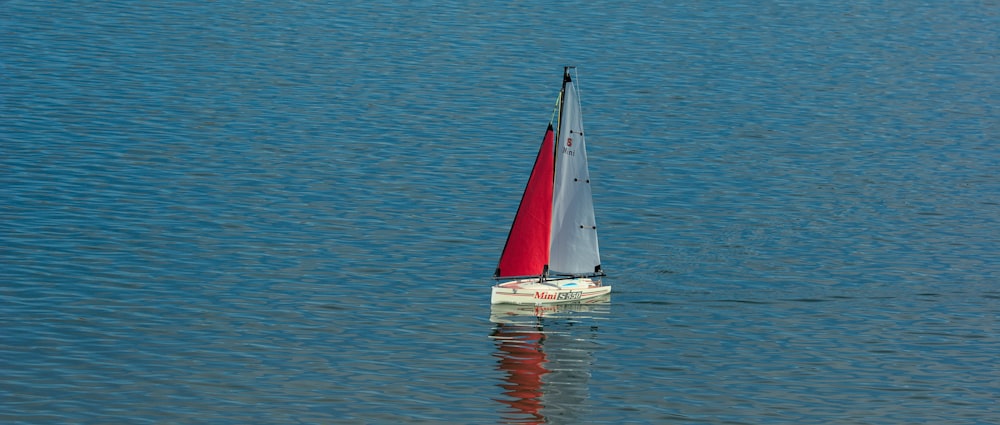 a red and white sail boat floating on top of a body of water